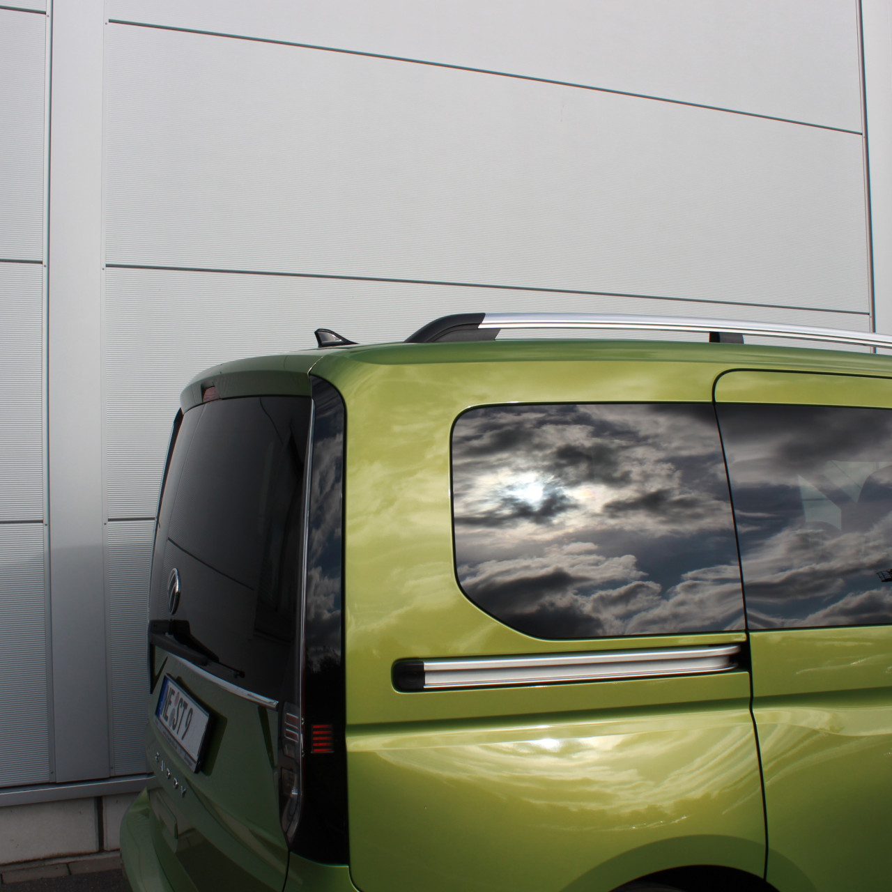 Das Heck eines grünen VW Caddy vor einem Gebäude